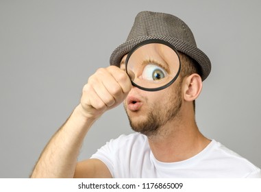 Astonished man looking through a magnifying glass on gray background