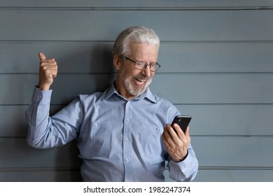 Astonished old grey haired man in eyeglasses holding smartphone looking happy celebrate great news pose in studio on blue wooden background. Sale, commercial offer, auction, moment of victory concept - Powered by Shutterstock