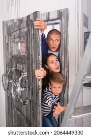 Astonished And Scared Young Man And Woman With Two Teen Boys Trying To Get Into Room Through Heavy Steel Bunker Door With Handwheels Of Locks. Reality Quest, Role Play And Family Fun Concept