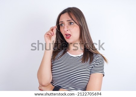 Astonished young Arab woman wearing striped t-shirt over white background looks aside surprisingly with opened mouth.