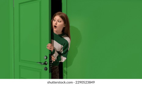 Jovencita sorprendida, adolescente mirando por la puerta verde con la cara conmocionada, mirando con los ojos abiertos. Sorpresa. Concepto de emociones, expresión facial, estilo de vida, juventud