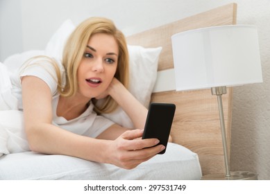 Astonished Young Woman In Bed Holding Mobile Phone - Powered by Shutterstock