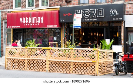 Astoria, New York, USA - 30 July 2020: People Eating At Tables Placed In City Street Surrounded By Wood Barricade In Astoria Queens Because Of New York Pause During COVID-19 Pandemic 2020.