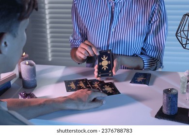 Astrologer predicting client's future with tarot cards at table indoors, closeup