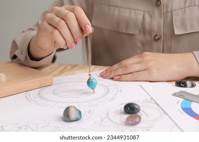 Astrologer using natal chart and pendulum for making forecast of fate at table, closeup. Fortune telling