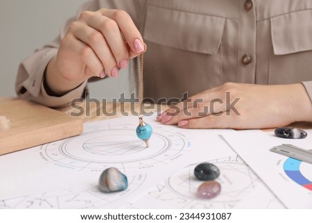 Astrologer using natal chart and pendulum for making forecast of fate at table, closeup. Fortune telling