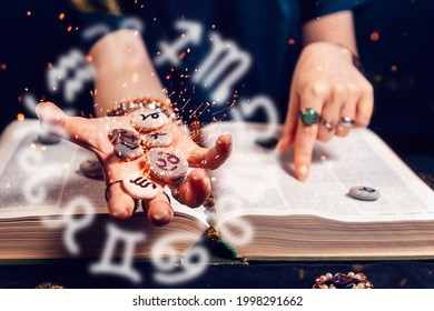 Astrology and horoscope. Fortune teller's hand holds the sparkling zodiac stones in the palm of her hand over the open book. The concept of divination and magic. - Shutterstock ID 1998291662