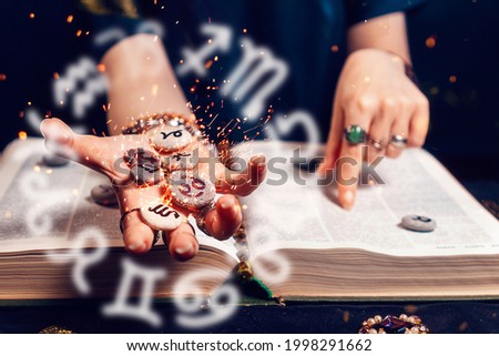 Astrology and horoscope. Fortune teller's hand holds the sparkling zodiac stones in the palm of her hand over the open book. The concept of divination and magic.