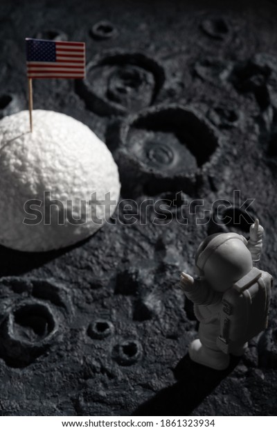 astronaut cheering up and facing\
the American flag on a planet with craters at vertical\
composition