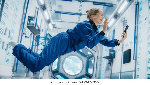 Astronaut Floating in Zero Gravity on Board a Spacecraft. Female Having a Video Call with a Family or Friends From Planet Earth. Engineer Using Smartphone in Space Inside an Orbiting Spaceship - Powered by Shutterstock