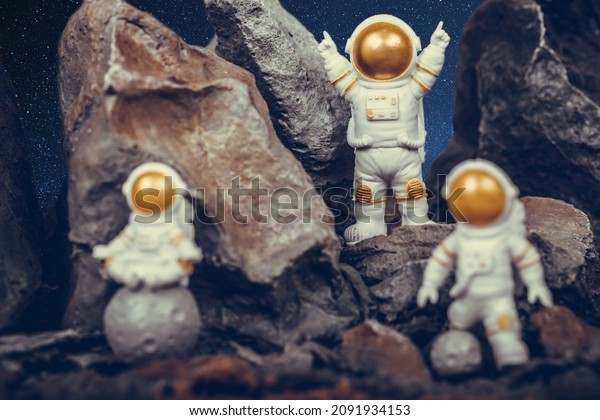 Astronaut with\
gold visor and White Spacesuit on rock surface with space\
background. One astronaut on the moon sitting and meditating while\
another astronauts celebrating\
success.