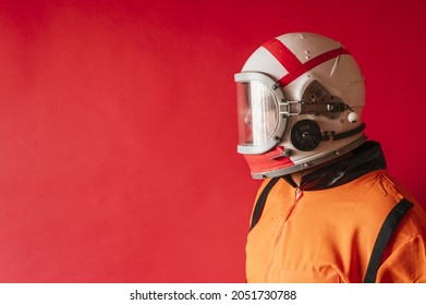 An Astronaut With A Helmet And An Orange Space Suit On A Red Background With Copy Space