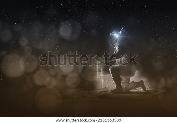 An\
astronaut on the moon sits on one knee above the craters and holds\
the soil in his hand. Space exploration concept. Dark template for\
light text. Elements of this image furnished by\
NASA.