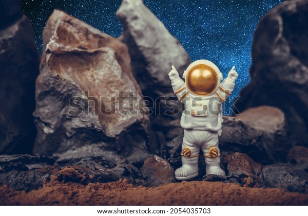 Astronaut raising arms while\
standing on rocky mountain. Spaceman wearing white space suit and\
helmet. Concept of cosmonautics, space travel, freedom and\
winning.