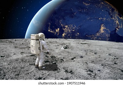 An astronaut standing on the surface of the moon looking up to the earth on the background. Elements of this image furnished by NASA. - Shutterstock ID 1907511946