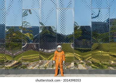 Astronaut Wearing Orange Spacesuit And Space Helmet Near A Huge Mirror Wall