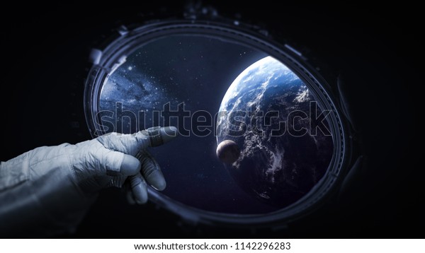Astronauts hand near porthole of space station.\
Earth, Moon and galaxy on background. Elements of this image\
furnished by NASA