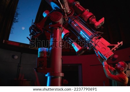 Astronomer with a big astronomical telescope in observatory doing science research of space and celestial objects.