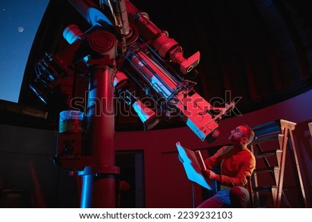 Astronomer with a big astronomical telescope in observatory doing science research of space and celestial objects.