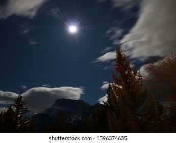 An Astrophotography Image. Long Exposure At Night During Full Moon. Clouds And Trees Deliberately Blurred With Focus On The Mountain And Features Both Moon And Pinpoint Stars. No Star Trailing.