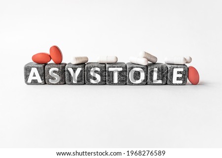 ASYSTOLE the word on stone cubes. Cubes stand on a white surface, many white and red pills. Medicine concept. absence of electrical activity in the heartm, death
