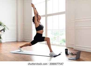 Atheltic Young Woman Doing Forward Lunges Exercise With Arms Overhead Watching Online Workout Video Tutorial Training At Home, Standing In 1 Warrior Pose On Yoga Mat. Domestic Female Fitness Concept