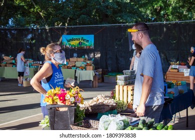 Athens, Georgia - September 5, 2020: During The COVID-19 Pandemic, A Customer Wearing A Face Mask Talks With A Vendor Wearing A Clear Face Shield At The Athens Farmers Market.