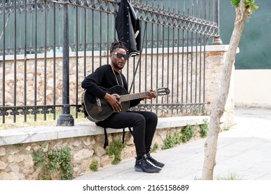 Athens, Greece, 04.30.2022. A Black Street Musician Sits Along The Sidewalk And Plays The Guitar.