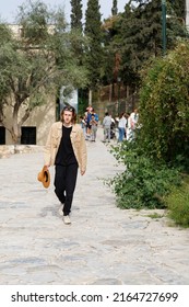 Athens, Greece, 04.30.2022. A Man With Medium Length Hair In A Beige Shirt And A Hat In His Hand Walks Through The City Of Athens.