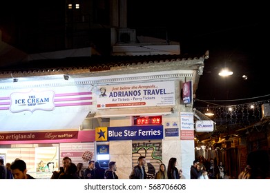 ATHENS, GREECE - 26 MAR 2016: Busy Monastiraki Square With Ice Cream Shop, Travel Agency And People Walking At Night On The Street Pl. Monastirakiou