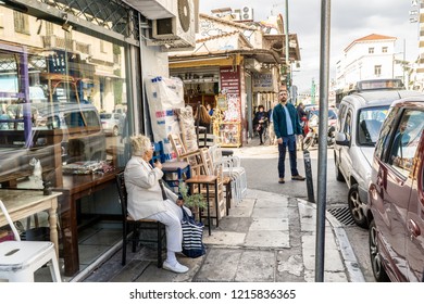 Athens, Greece - October 14, 2018: Busy Street Scene In Monastiraki, A Neighborhood Known For Its Flea Market And Shopping Opportunities - A Woman Sits To Rest On The Sidewalk While Out Shopping.