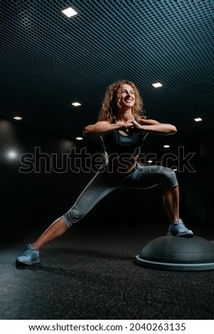 Athlete in black colored gym is engaged in fitness doing squats on a balancing platform for deep muscles. Concept of weight loss.
