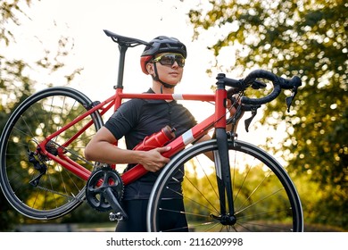 athlete caucasian competitor cyclist carrying bicycle in hands, in nature on road, wearing sportive outfit, in glasses and helmet. sport, fitness, workout, training, healthy lifestyle concept - Powered by Shutterstock