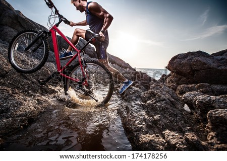Athlete crossing rocky terrain with water barrier with his bicycle