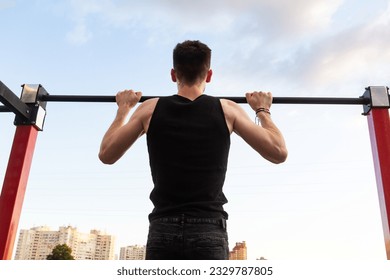 Athlete doing pull-up on horizontal bar. Muscular man doing exercise pull ups on horizontal bar in park, outdoor workout - Powered by Shutterstock