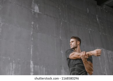 Athlete doing stretching warmup exercise. Male fitness model in fashion sportswear in city. Runner sprinting on urban gray background. Sport, workout, healthy lifestyle concept.