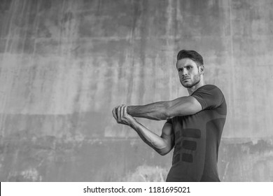 Athlete doing stretching warmup exercise. Male fitness model in fashion sportswear in city. Runner sprinting on urban gray background. Sport, workout, healthy lifestyle concept. Black and white.