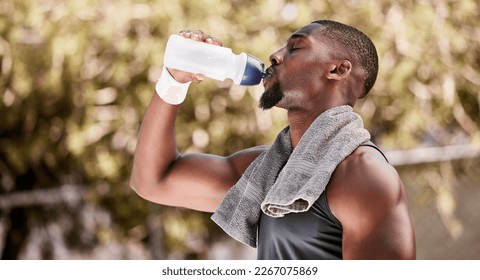 Athlete drinking water from a bottle during an outdoor workout. Fit, athletic african american man taking break to hydrate and refresh while standing alone outside. Routine exercise for health - Powered by Shutterstock