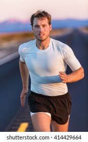 Athlete Endurance Runner Man Long Distance Running With Focus And Determination On Desert Road At Sunset. Sportsman Training In Compression Sports T-shirt And Shorts Activewear In Summer Landscape.