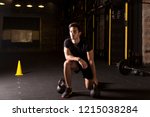 Athlete exercising kettlebell drills at the gym. Dark photography concept with dumbell and kettlebell background.