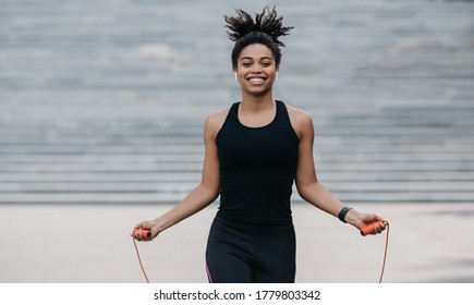 Athlete Exercising Outside In Sunny Park. Smiling African American Girl In Sportswear Training With Jumping Rope On City Staircase Background, Free Space