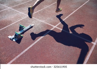 Athlete In Gold Shoes Sprinting From The Starting Blocks Over The Starting Line Of A Race On A Red Running Track 