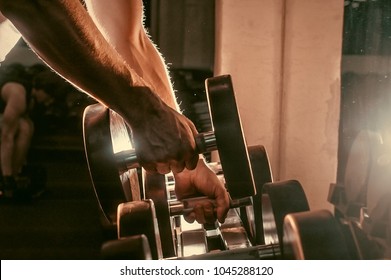 Athlete in the gym training with dumbbells. Toned image. Man is engaged with dumbbells on the bench. Hands with dumbbells. another view close