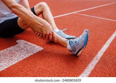 Athlete holding his leg injured after running at track and field stadium after jogging, running competition, sports injury concept - Powered by Shutterstock