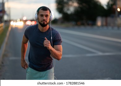 An athlete jogs through the city at night, a man runs in the evening on the road - Powered by Shutterstock