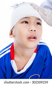 Athlete Little Asian (thai) Boy In Blue Sportswear With Trauma Of The Head. Doctor Makes A Bandage On Head Patient. Child Unhappy, On White Background