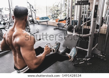 Athlete makes low cable pulley row seated in gym. Close back view