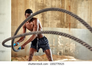 Athlete man with a battle rope doing sports exercises outdoor. Black male athlete exercising, doing functional fitness training with heavy rope