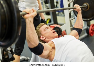 Athlete Man Does Bench Press Exercise In Gym Hall Under Supervision Of Female Coach