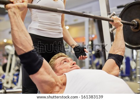 Athlete man does bench press from chest exercise in gym hall under supervision of female coach